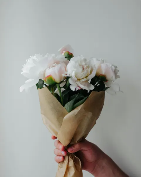 Une main tient un bouquet de fleurs blanches dans un papier kraft