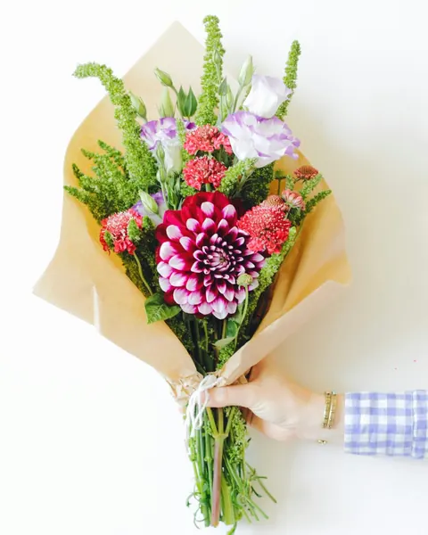 Un bouquet champêtre dans du papier kraft : dahlia pourpre, œillets, lisianthus et épis verts