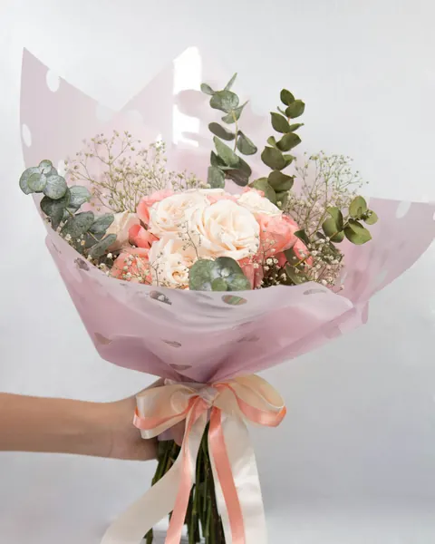 Un bouquet de roses poudrées, gypsophile et eucalyptus dans un papier rose noué d’un ruban
